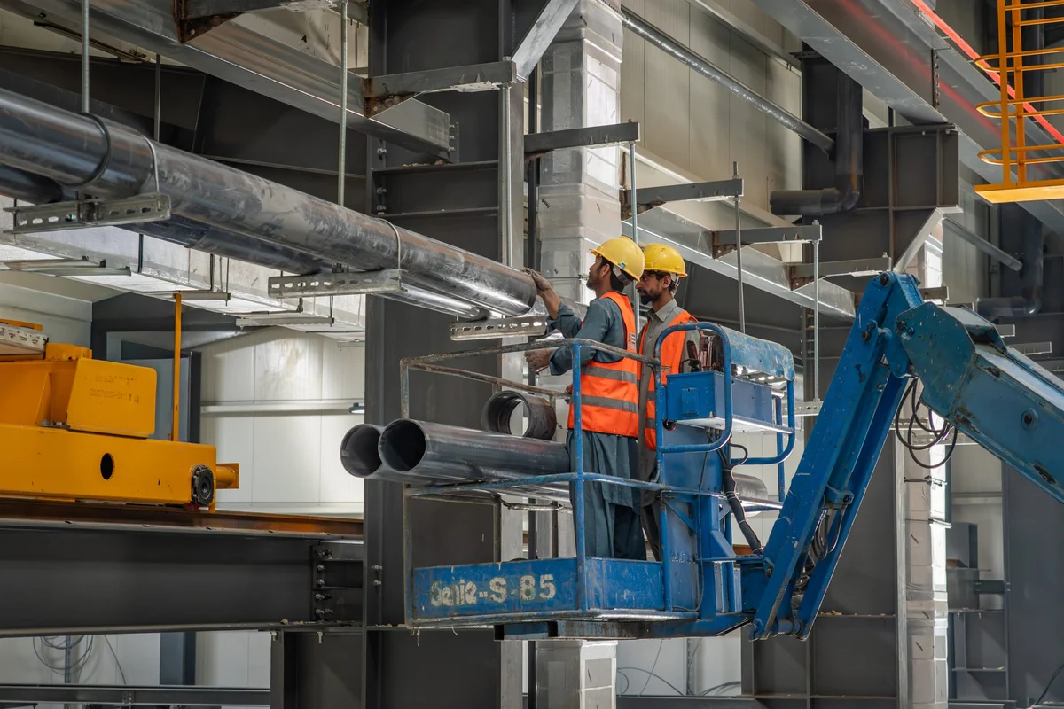 Engineers installing overhead ventilation ductwork inside an industrial building