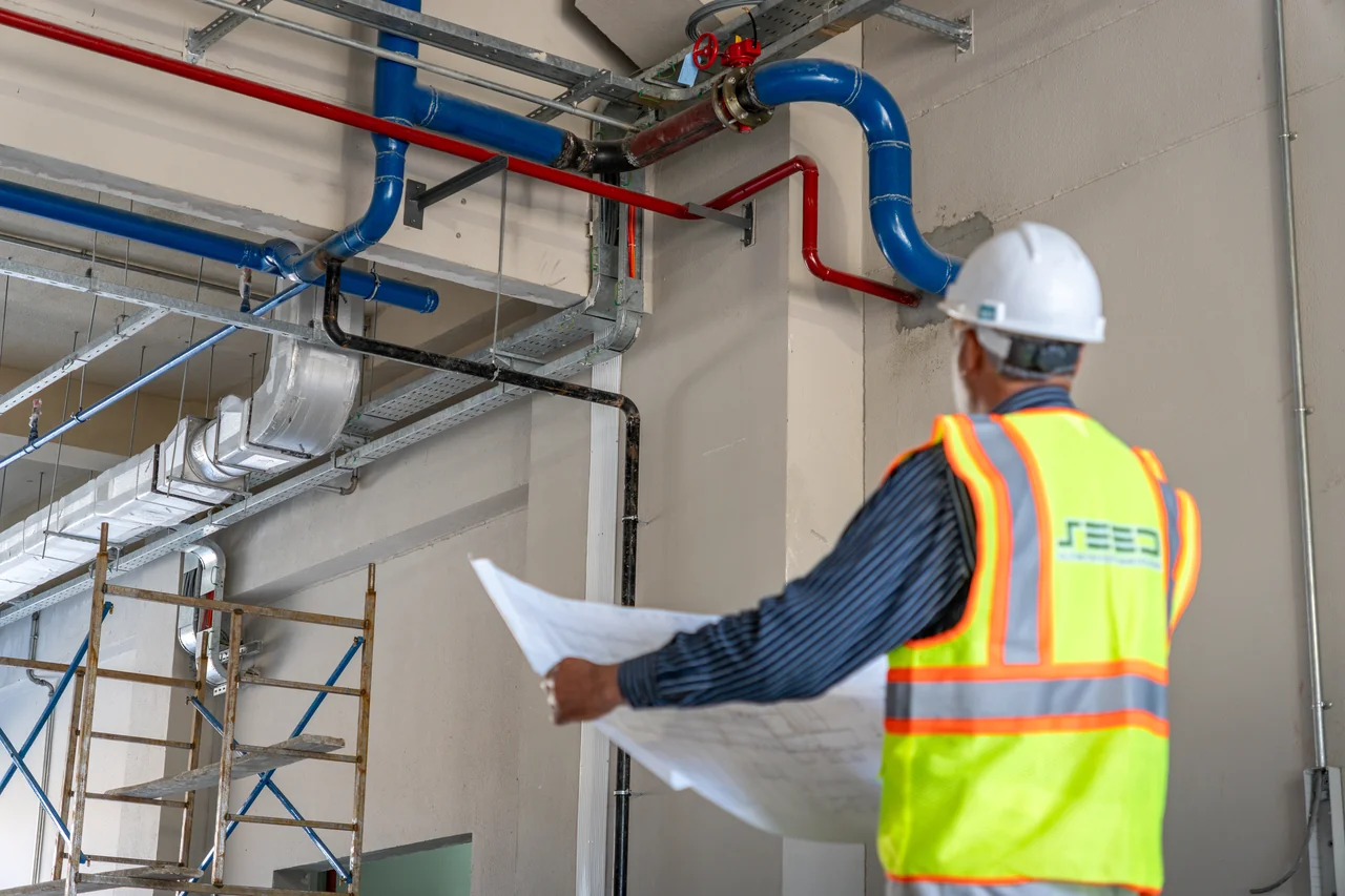 SEED site team member reviewing drawings beside installed pipework at Wah